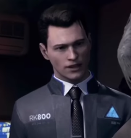 a closeup shot of connor, an android character from the video game detroit: become human. he is wearing a gray jacket with "rk800" printed on it over a white shirt and tie. he has short, dark hair and is looking slightly to the left of the camera with his mouth slightly open as if he is speaking. the background is dark and blurry.