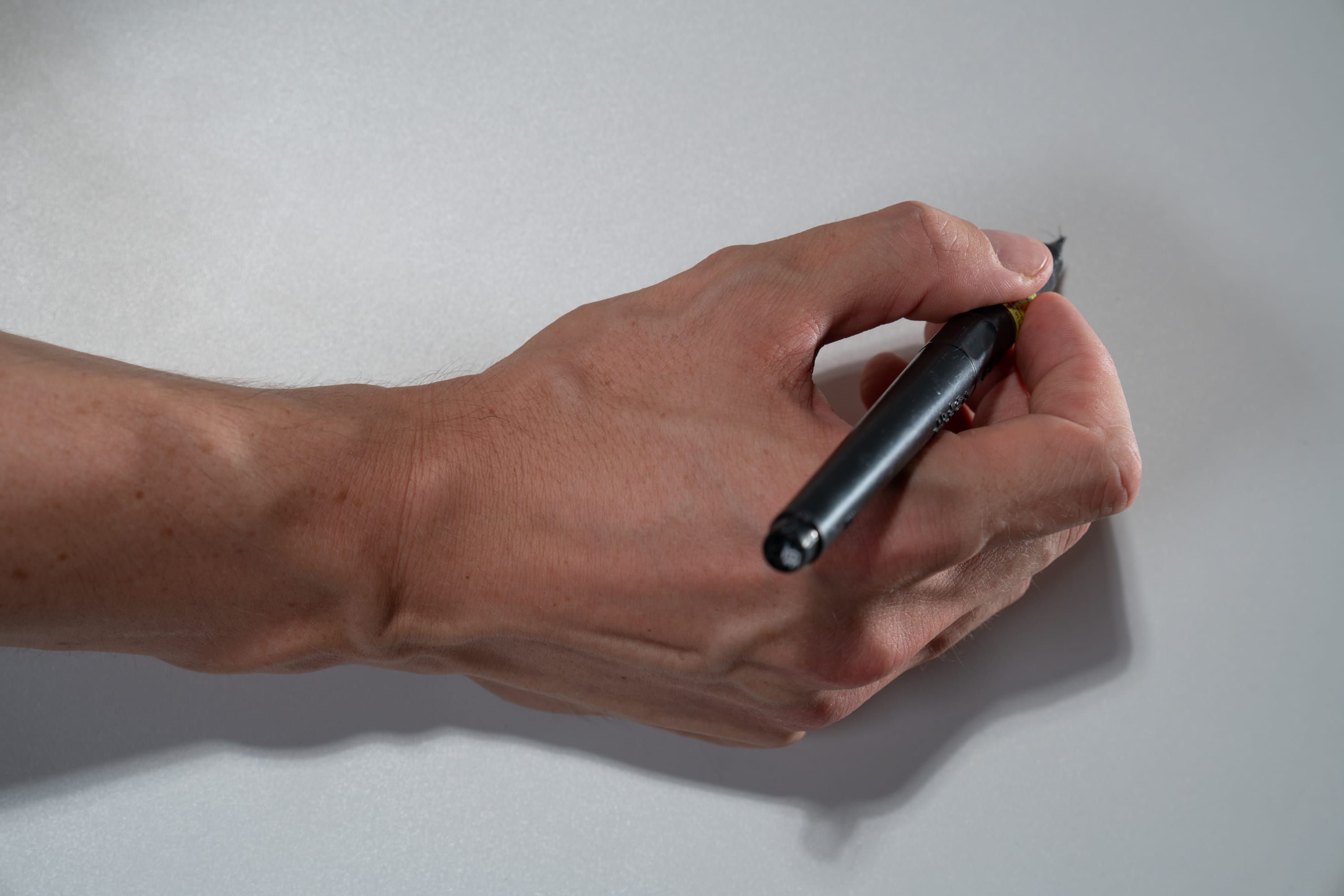 a hand is holding a black pen and writing against a white background.