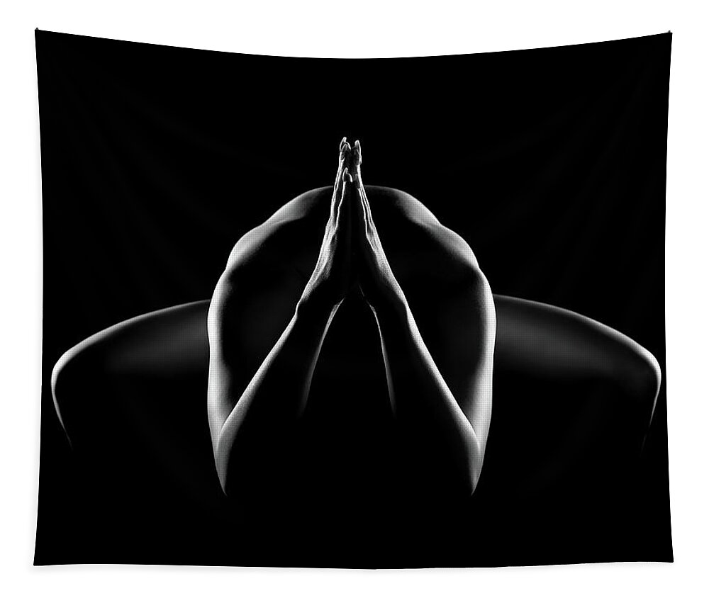 the image is a black and white photograph of a woman's nude body.  she is positioned in a crouched or seated pose with her hands clasped together in a prayerlike gesture in front of her chest. the lighting is dramatic, creating strong contrasts between light and shadow, and the focus is entirely on the form and pose of the body, with details obscured by the dark background.  the overall mood is serene and contemplative. the style is reminiscent of fine art photography and suggests themes of spirituality, meditation, or introspection.