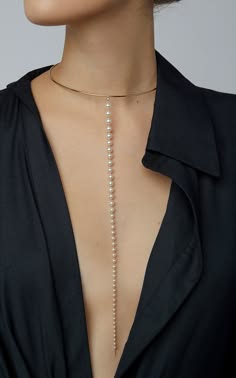 a woman wearing a black collared shirt with a gold choker and a long pearl necklace. the pearl necklace hangs down from the choker, reaching past her chest. the woman has a neutral expression on her face. the image is shot from the chest up and focused on the jewelry.  she is styled with a sleek, minimalist look with a delicate and elegant necklace.  the overall image exudes style, sophistication and timeless beauty.