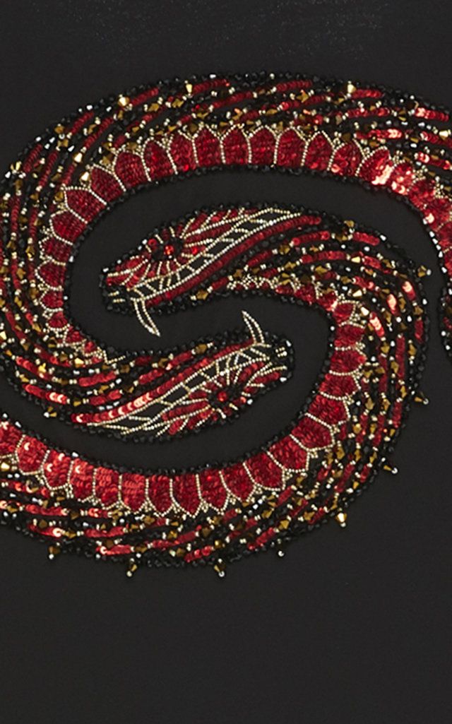 the image shows a closeup of a coiled snake design embroidered with beads and sequins on a black background. the snake is primarily red with black and gold accents. there are two snake heads visible, each with embroidered details and pointed fangs. the design appears to be part of a larger textile or garment.