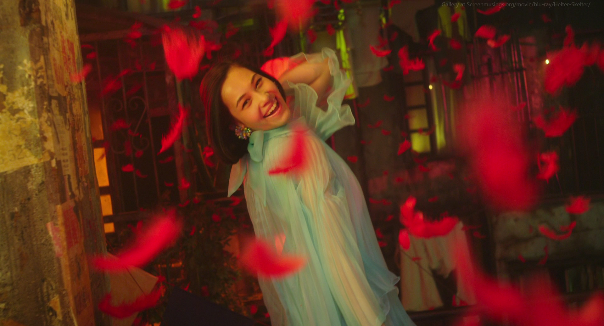 a beautiful young woman in a light blue dress is laughing and smiling as she walks through a room filled with falling red petals. the room is lit with warm yellow light, creating a dreamy and romantic atmosphere. the woman's hair is long and dark, and she has a beautiful smile on her face. the red petals falling around her create a magical and whimsical effect.