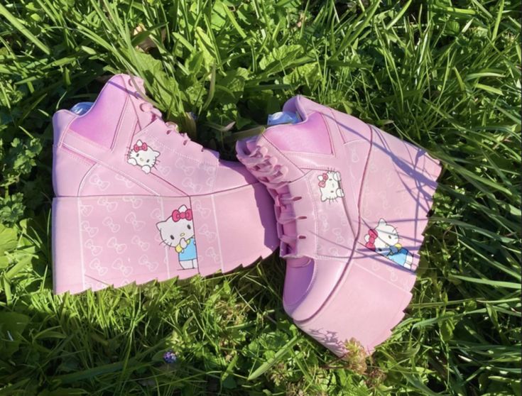 a pair of pink hello kitty platform sneakers are sitting in green grass. each shoe has hello kitty designs on it.