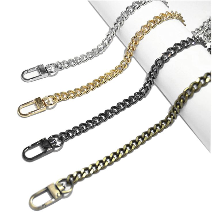 four chains, one silver, one gold, one black, and one bronze are lying on a white surface. each chain has a clasp on one end.