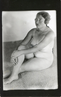 a black and white photograph of a nude woman seated on a textured surface. the woman appears to be from the 1920s or 1930s, based on her hairstyle and the overall style of the image. she is posed in a relaxed, almost contemplative manner, looking slightly away from the camera. the lighting and focus create a soft, intimate mood. the background is a textured surface that adds depth to the image.  the photograph has a vintage feel, suggestive of a studio portrait.