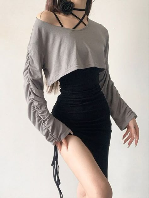 a young woman wearing a stylish outfit is standing in front of a white wall, looking away from the camera. she's wearing a grey crop top with long sleeves, a black skirt with a side slit and a drawstring, and a black choker with a black rose attached to it. her hair is styled in a loose wave and she's wearing light makeup.