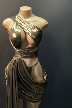a female mannequin in a gold metallic dress is posed elegantly, with a one shoulder neckline, a flowing, draped fabric and a form fitting design that accentuates her figure.  the dress appears to be made of a luxurious fabric, and the model is posing in a classic, glamorous way. the background is a dark, simple backdrop, which allows the dress to be the center of attention.