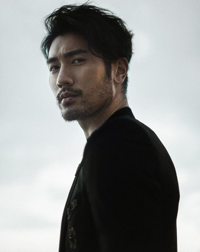 a portrait of an asian man with dark hair and a wellgroomed beard. he is wearing a black jacket and looking directly at the viewer. the background is a blurred light grey.