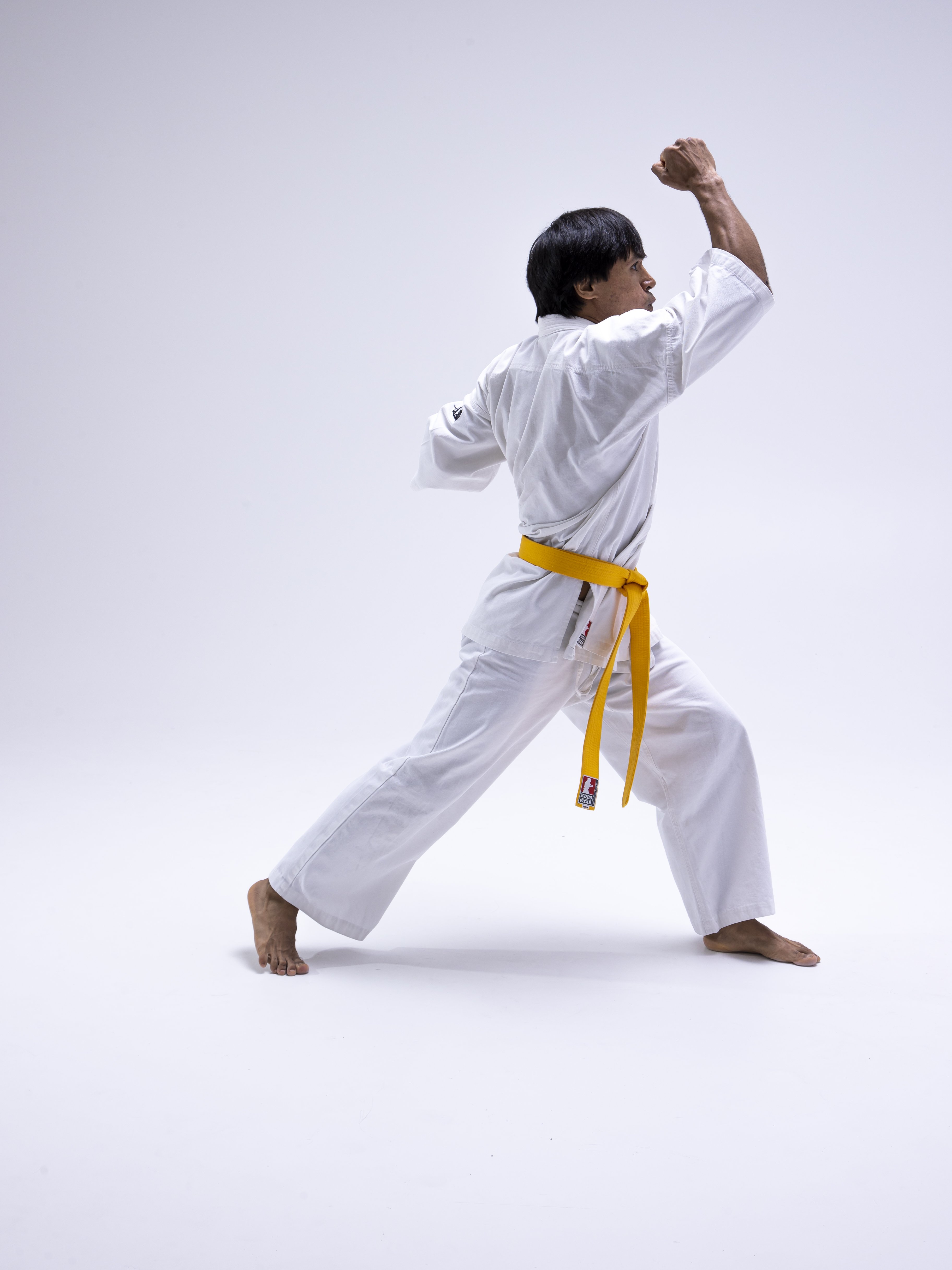 a man in a white karate uniform with a yellow belt stands barefoot in a martial arts stance, his fists clenched.
