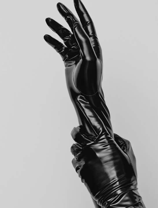 a pair of black leather gloves are worn on a person's hands. the gloves are long and reach up to the elbows. the gloves are made of a shiny material that appears to be latex. the hands are in a posed position, with the fingers extended and the palms facing the camera. the photo is taken against a white background.