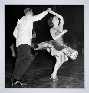 a man and woman dancing in a ballroom. the man is wearing a suit and tie, and the woman is wearing a long dress. they are both smiling and seem to be enjoying themselves. the photo was taken in black and white, and it has a vintage feel.