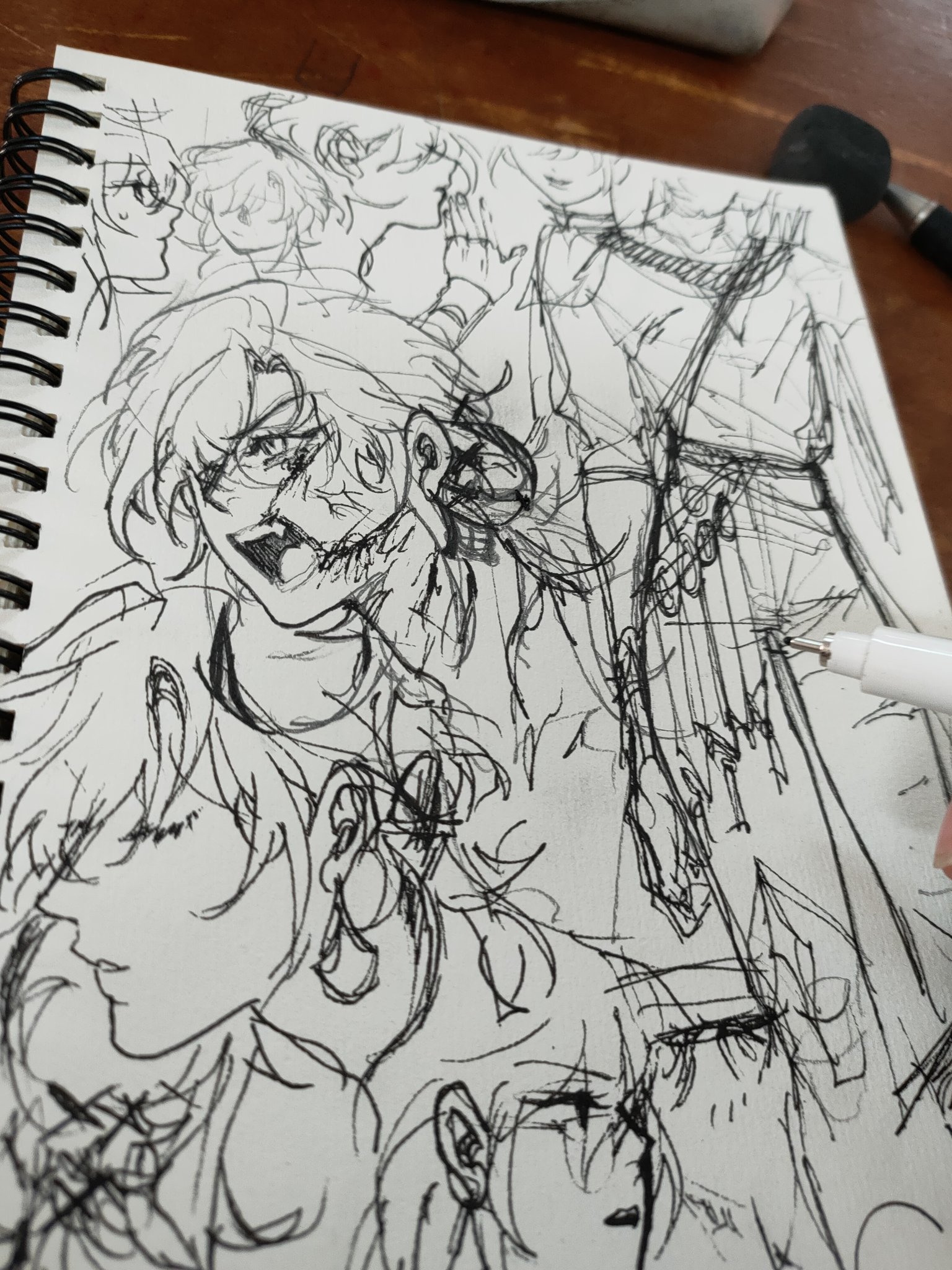a closeup shot of a sketchbook page filled with a variety of messy, expressive ink drawings.  the style appears to be influenced by anime or manga, featuring multiple characters with exaggerated features and hairstyles.  some figures are more fully realized than others, with a mixture of detailed faces and quickly sketched forms. the drawings are overlapping and layered, creating a sense of dynamism and spontaneity. a pen is visible in the lower right corner, suggesting the drawing is in progress. the overall impression is one of casual creativity and expressive linework.