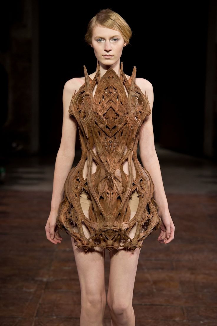 a fashion model walks down the runway in a unique, futuristic dress that appears to be made of intricately carved wood.  the dress is a statement piece that is sure to turn heads and is a testament to the creativity of fashion designers.