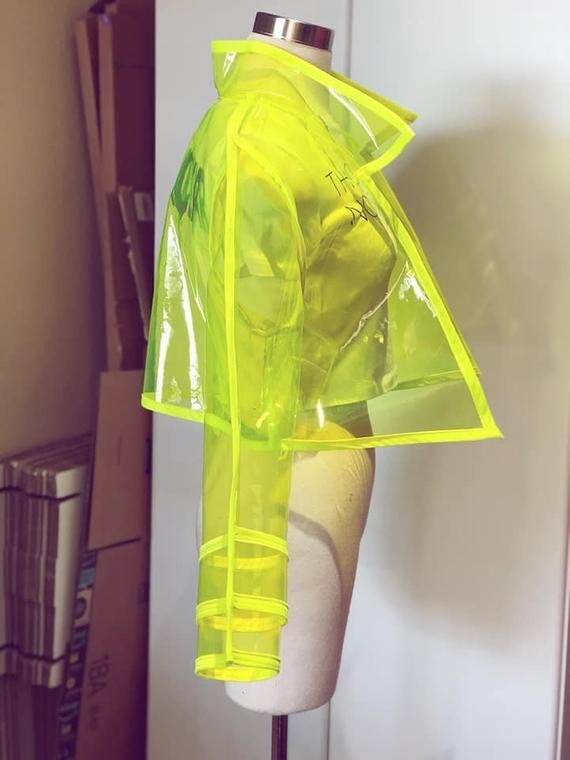 a neon yellow plastic raincoat on a mannequin. the jacket is transparent and has a cropped silhouette.  the jacket is accessorized with a neon yellow trim.