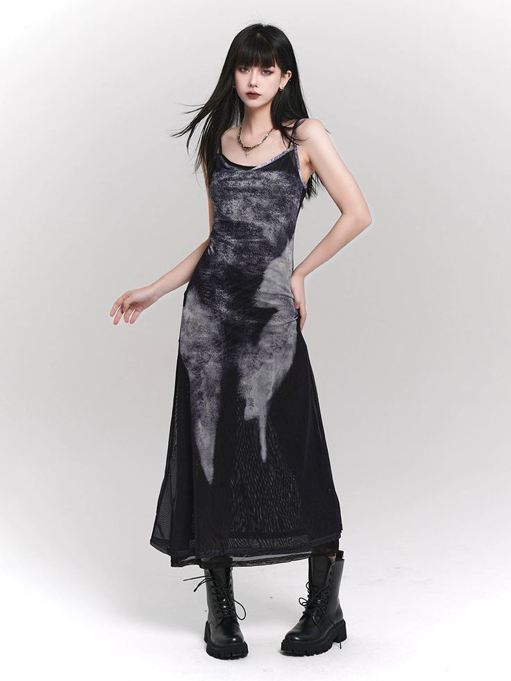 a fulllength studio shot of a young woman modeling a long, dark gray and black tiedye maxi dress made of sheer mesh material. the dress has thin spaghetti straps and a relaxed fit.  she is wearing black combat boots and a simple necklace. the background is plain white. the overall style is gothic or dark fashion with a grunge influence. the model's hair is dark and straight, and her makeup is fairly neutral.
