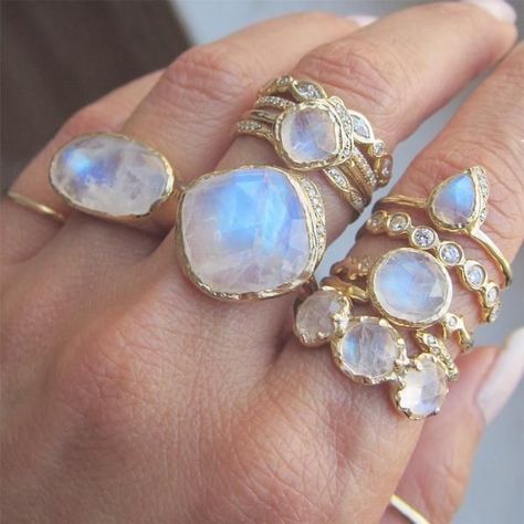 close up of a woman's hand with multiple gold rings featuring moonstones. the hand is held up, showcasing the rings in good lighting.