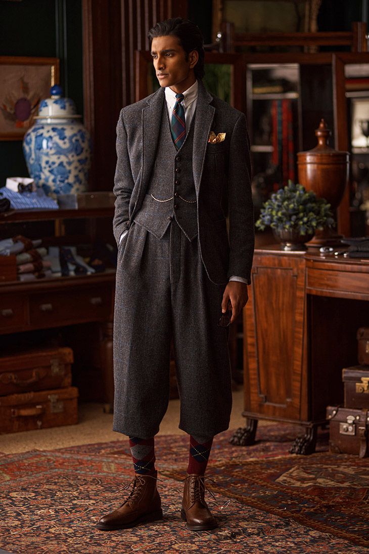 a fullbody shot of a male model dressed in a stylish threepiece tweed suit. the suit features plus fours or knickerbockers, and is complemented by argyle socks and brown brogues. he is standing in an antiquefilled room, conveying a vintage or retro vibe. the image emphasizes classic style, elegance, and sophistication.