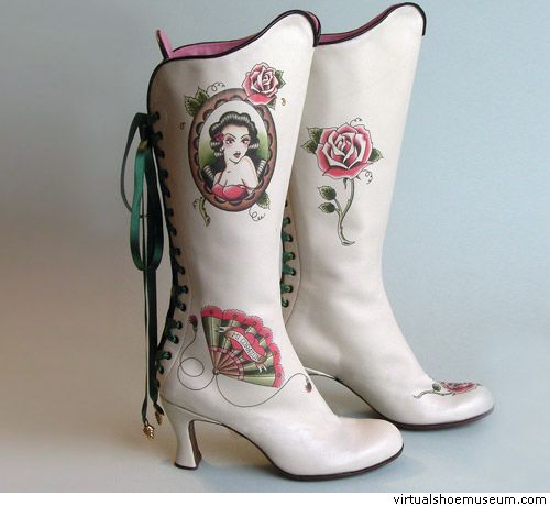 a pair of white, kneehigh heeled boots with decorative tattoostyle designs are displayed. one boot features a portrait of a woman in an oval frame, a rose, and a fan design near the ankle. the other boot is decorated with a rose near the top and a smaller flower on the toe. green ribbons are laced up the back of one boot.