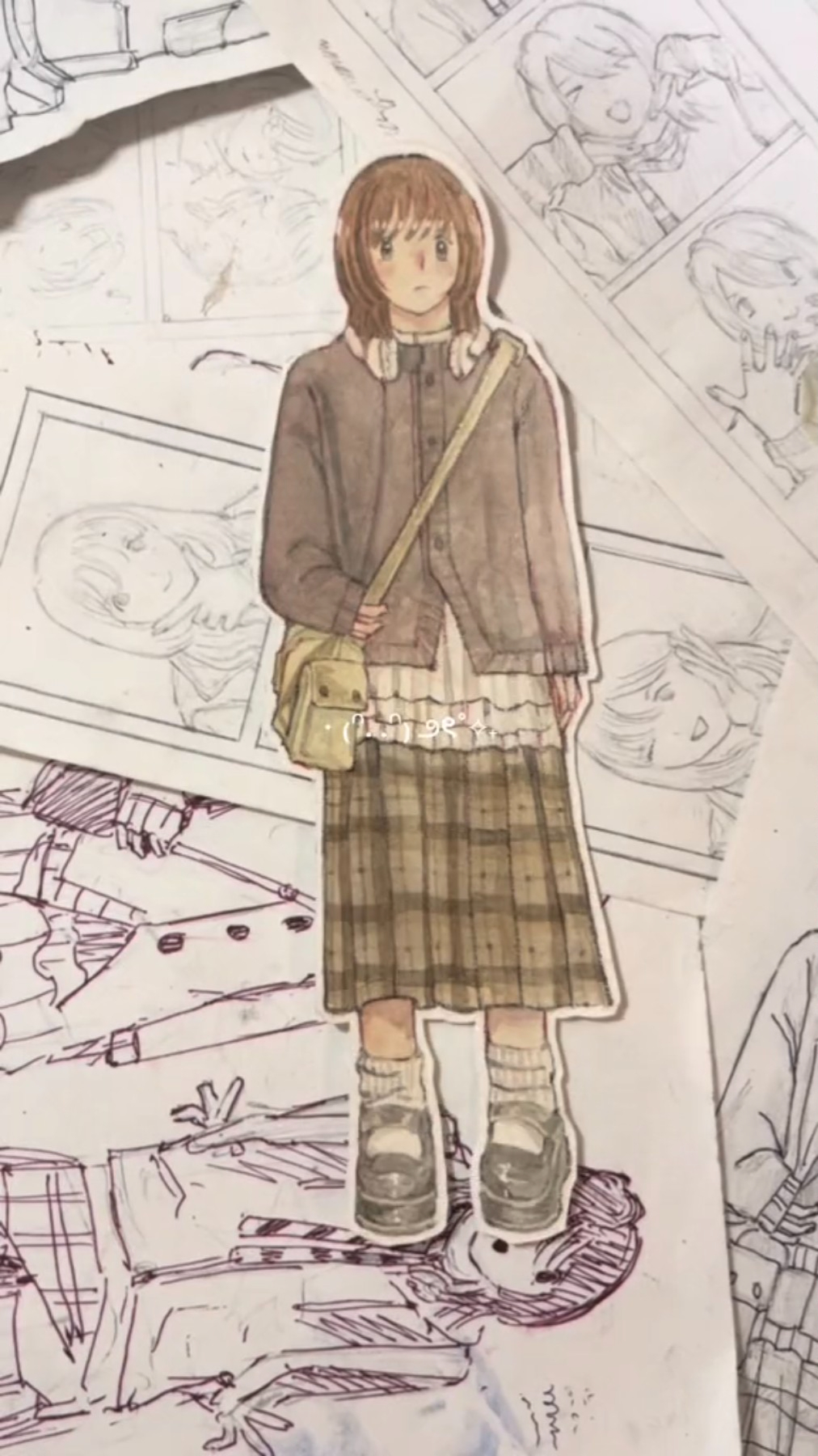 a drawing of an anime girl in a brown and white outfit. she is wearing a plaid skirt, brown boots, a brown cardigan, and a white top. she has long brown hair and a bag over her shoulder. the drawing is on a piece of paper with other drawings on it. the drawing is done in pencil and colored with markers. the style is cute and casual.