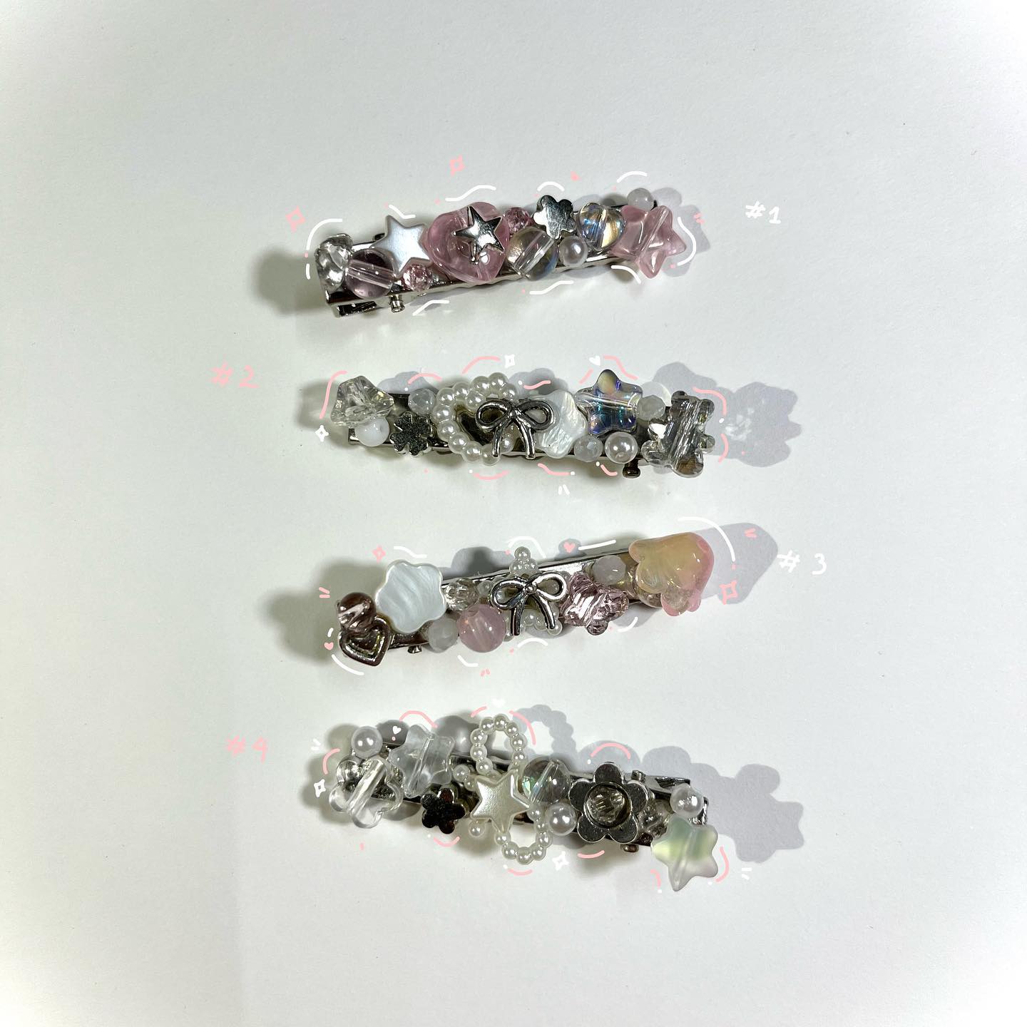 the image shows four hair clips adorned with various beads, stars, hearts, and bow charms. the first clip is pinkthemed, the second and fourth are white and silverthemed, and the third has a pink and peach color scheme. they are laid out on a white surface with soft shadows.