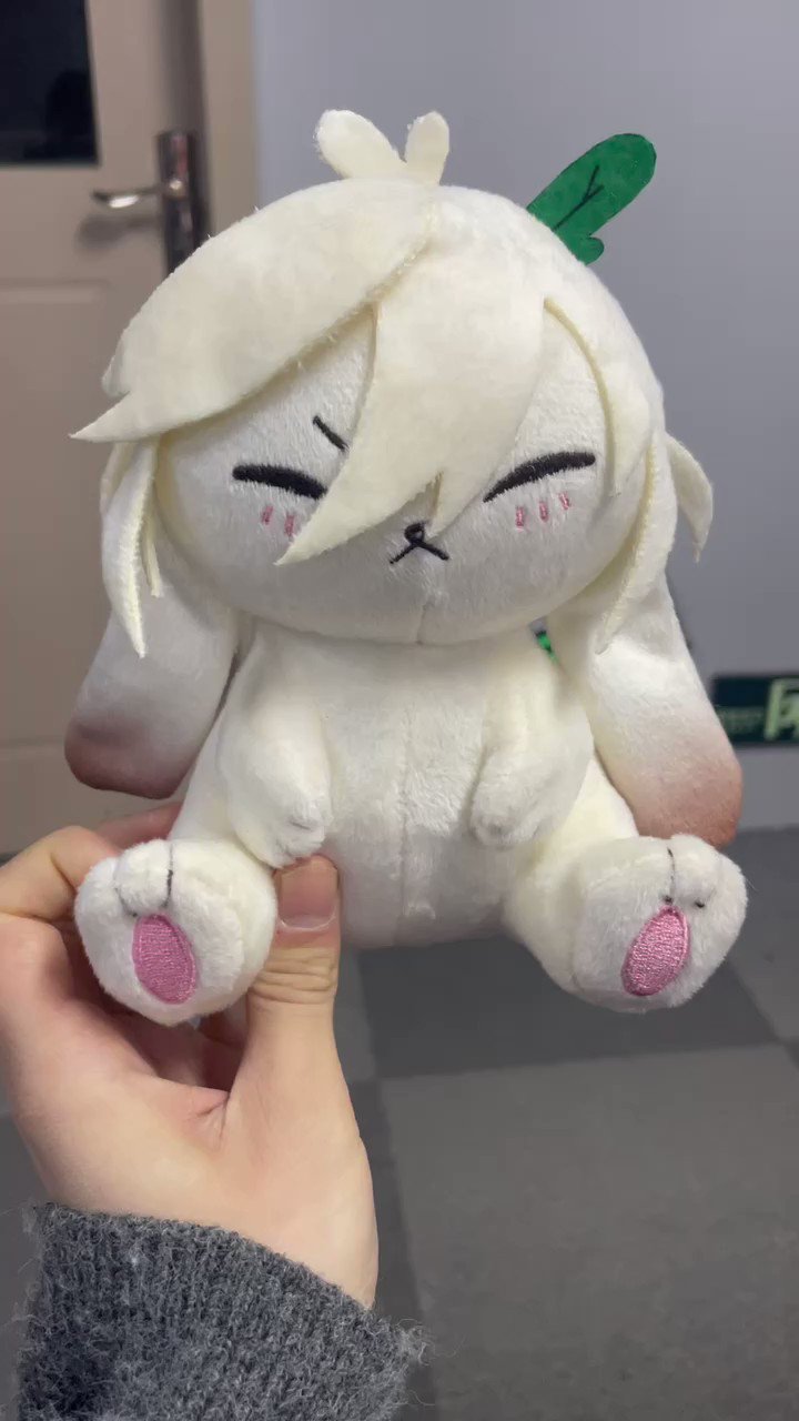 a soft white bunny plush toy with a green leaf on its head. the bunny has a cute expression and a little pink nose.  a person is holding the bunny in their hand.