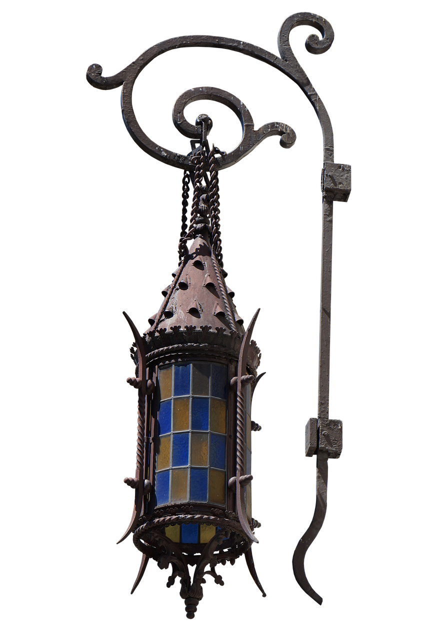 the image shows an ornate, antique light fixture against a black background. it appears to be a hanging lantern made of iron and metal, with decorative elements. the lantern has glass panels with a pattern of blue and yellow squares. the ironwork is detailed and features curved shapes and twisted patterns. the fixture is mounted on a metal arm that extends from a vertical post. the overall style is oldfashioned and architectural.