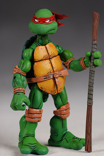 the image shows a teenage mutant ninja turtles raphael action figure holding a staff. he is a retro collectible toy from the 1980s/1990s. he has green skin, a red mask, and a shell.