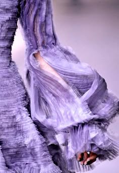 a closeup shot of a model wearing a purple dress with ruffled detailing. the dress is made of soft, flowing fabric, and has a delicate, feminine look. the model is posing with her arm extended, showcasing the beautiful texture and detail of the dress.  the image captures the elegance and sophistication of high fashion.