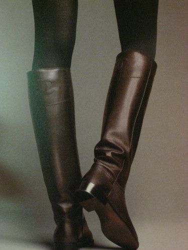 a woman in brown leather boots poses in a studio with her legs crossed. her boots are tall and have a high heel. they are stylish and sleek and have a classic look.