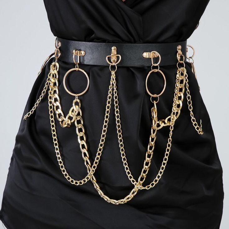 a black dress is cinched at the waist with a black leather belt adorned with gold chains and rings. the chains hang down from the belt, creating a layered and stylish effect. the dress is draped, adding texture and depth to the overall look.