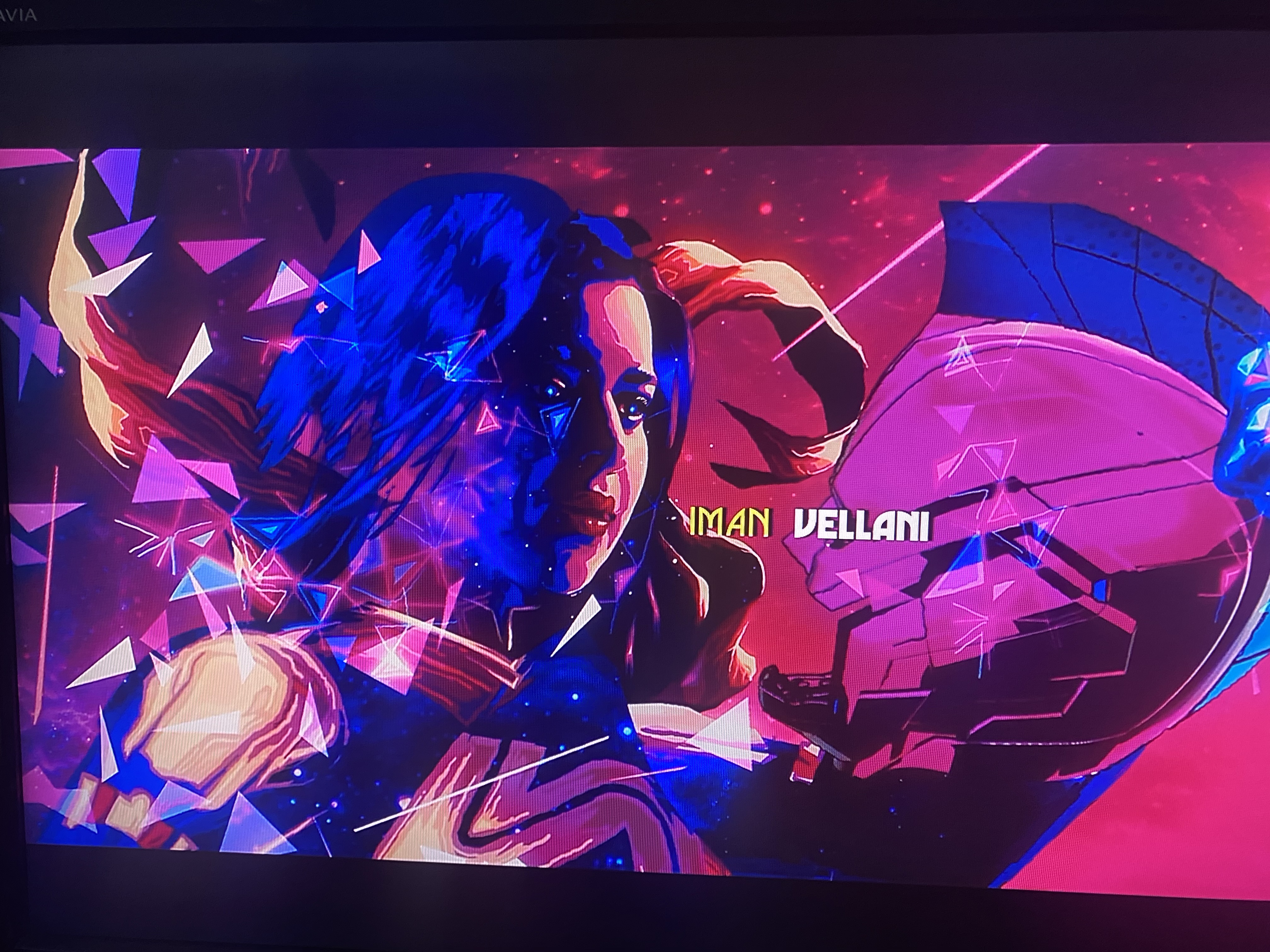 this is a poster for the disney+ show ms. marvel. the poster features a vibrant and colorful abstract design, with geometric shapes and neon colors. the central figure is ms. marvel herself, with her hair flowing in the wind and a determined look on her face. her signature red, blue, and yellow costume is visible, as well as a glowing aura that surrounds her. the background of the poster is a mix of pink, blue, and purple hues, with stars and geometric shapes that create a sense of motion and energy. the title "ms. marvel" is written in a bold, white font at the top of the poster. there is also a secondary title that reads "iman vellani" in a bright yellow color that is featured on the right side of the poster. this is a visually striking poster that captures the energy and excitement of the ms. marvel show.