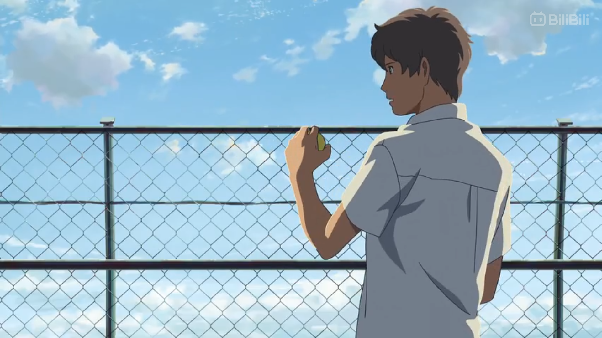 an anime boy in a white shortsleeved shirt, presumably a school uniform, stands facing away from the viewer. he holds a tennis ball in his right hand and is looking off to the right side of the frame. a tall chainlink fence is positioned behind him, separating him from a clear blue sky dotted with fluffy white clouds. the overall lighting suggests a bright, sunny day.