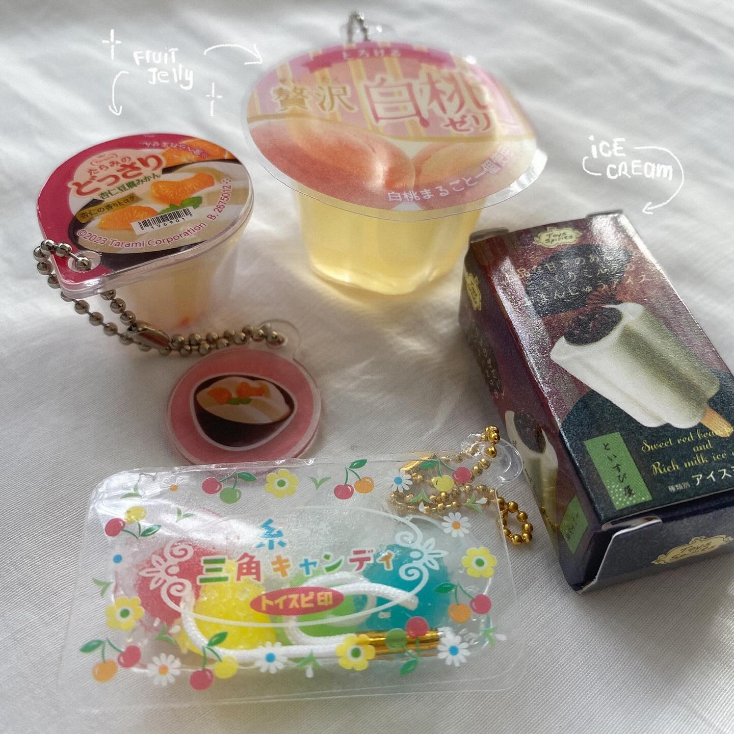 the image shows an assortment of japanese candy and desserts. there are two fruit jelly cups, one with mandarin oranges and another with white peaches. a package of triangular lollipops is also shown, alongside a box of ice cream. all items, except the ice cream, are attached with keychains.