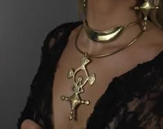 a woman wearing a gold necklace with a large pendant. she is wearing a black lace top. the necklace is close to her neck and the pendant is in the center of the image. the woman's skin is visible in the background and the pendant is in focus.  the woman is wearing a stylish outfit.