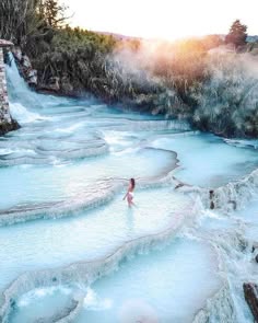 a woman wearing a white bikini walks through the crystal clear water of a blue hot spring in a natural setting.  the sun is shining, and the surrounding trees are green and lush.  the woman is enjoying the peace and tranquility of the natural hot spring.