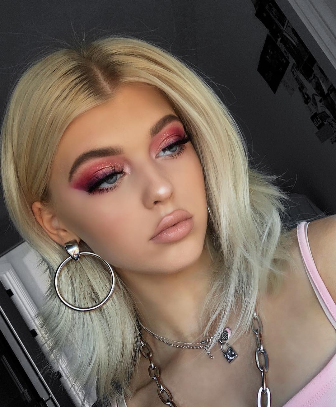 a portrait of loren gray with blonde hair and pink eyeshadow. she is wearing hoop earrings, necklaces, and a pink top. she has fair skin and is looking off to the side.