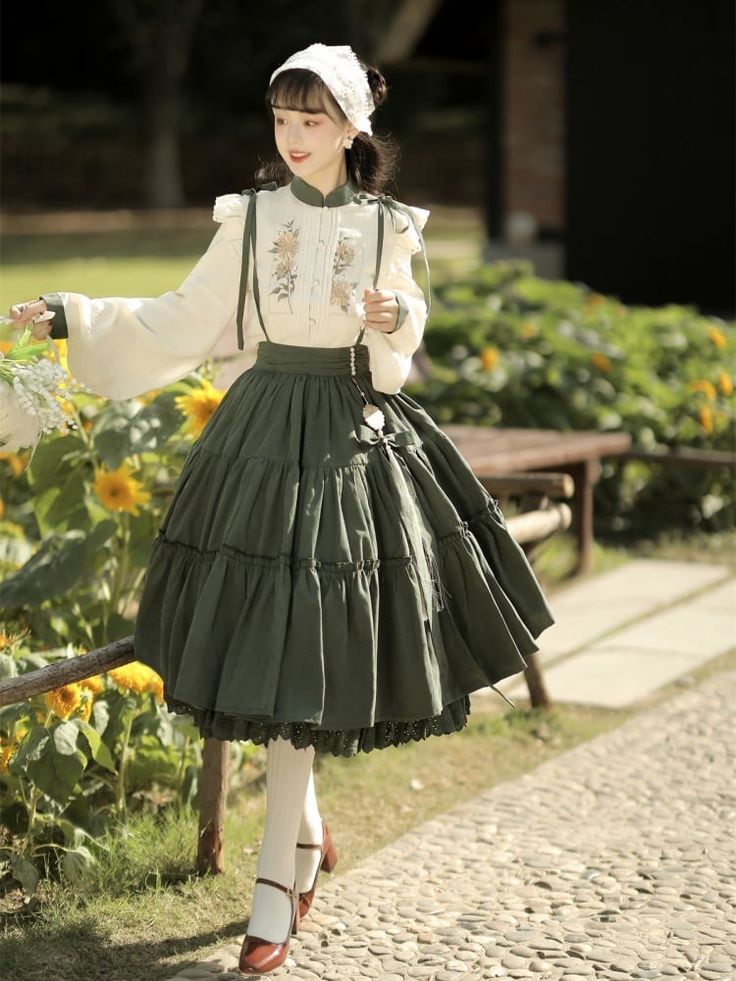 a young woman poses in a garden wearing a vintageinspired outfit. she is wearing a white embroidered blouse with puffed sleeves and a long green skirt. she is also wearing white stockings, brown mary jane shoes, and a white headscarf. she is holding a bouquet of flowers in her left hand.  the image is taken from an eyelevel perspective and the lighting is natural and sunny. the overall style of the image is cottagecore and lolita fashion.