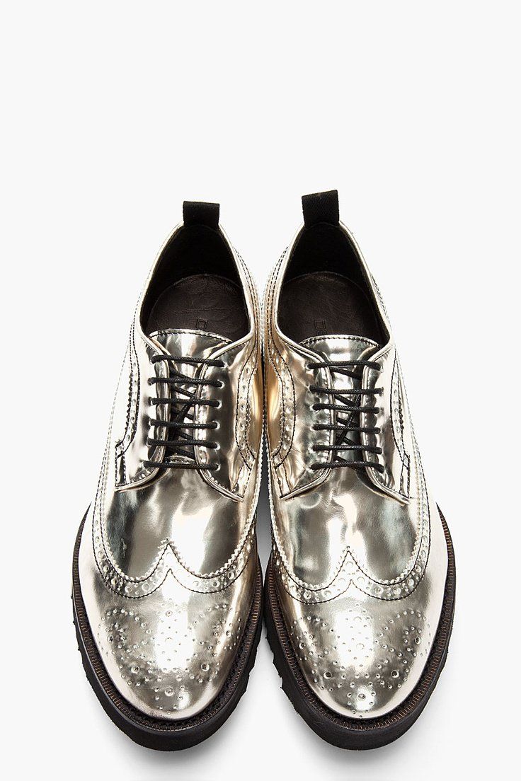 a pair of metallic gold brogue shoes are shown from a bird's eye view against a plain white background. the shoes are shiny and have black laces. they are pointedtoe oxfords with wingtip details and have a rubber sole.