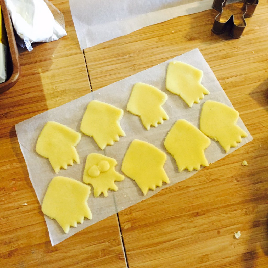 nine pieces of cutout squidshaped sugar cookie dough lay on a piece of parchment paper on a wooden table. there are other pieces of baking supplies on the table, including cookie cutters and more parchment paper.