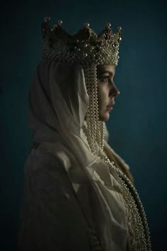 a portrait of a woman with a crown and a pearl necklace looking to the side.  the woman is dressed in an elegant white robe.  the background is dark with shadows.  the woman is looking to the side and appears to be in thought.