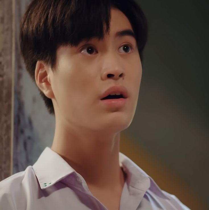 head and shoulders color photo of a young asian man with a surprised expression on his face. he has short, dark hair and is wearing a purple and white collared shirt. the background is dark and out of focus, making the man's face the central point of the image.