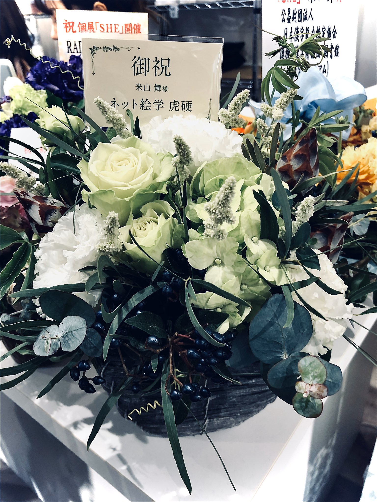 a flower arrangement with a card that says "congratulations" in japanese. the flowers are white and green. ```
