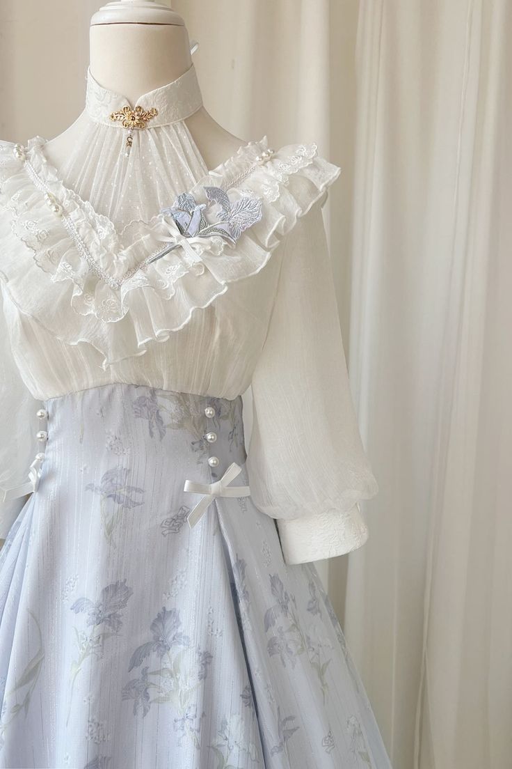 a delicate, highwaisted lolita fashion dress in a pale blue and white floral print. the dress features a white chiffon blouse with intricate lace detailing and delicate floral embellishments. the skirt is full and flowing, with a high waist and a row of pearl buttons down the front. the overall effect is one of ethereal beauty and romantic charm.