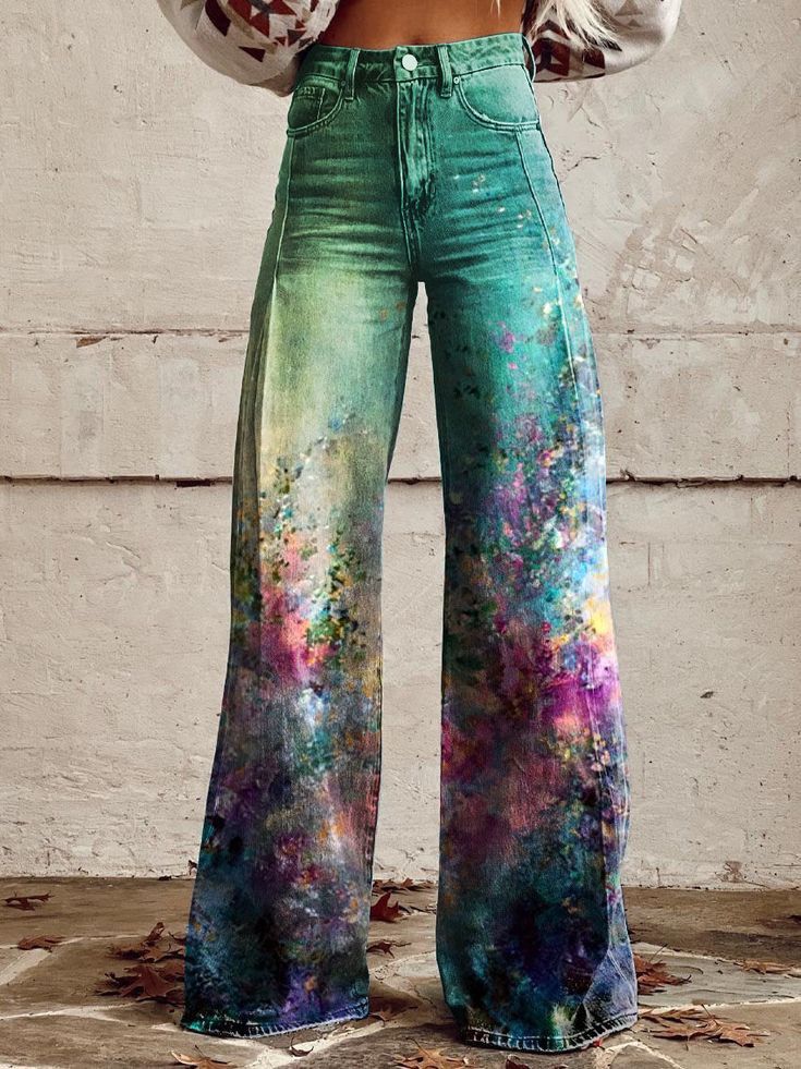 a woman is wearing a pair of wideleg, highwaisted jeans with a tie dye design in shades of green, purple, and blue. the jeans are flowing and the design is reminiscent of a floral print. she is wearing a white top that is tucked into the jeans, adding a casual and stylish look. the photo is taken in a nature setting with fallen leaves on the ground. the photo is welllit and shows off the details of the tie dye jeans.