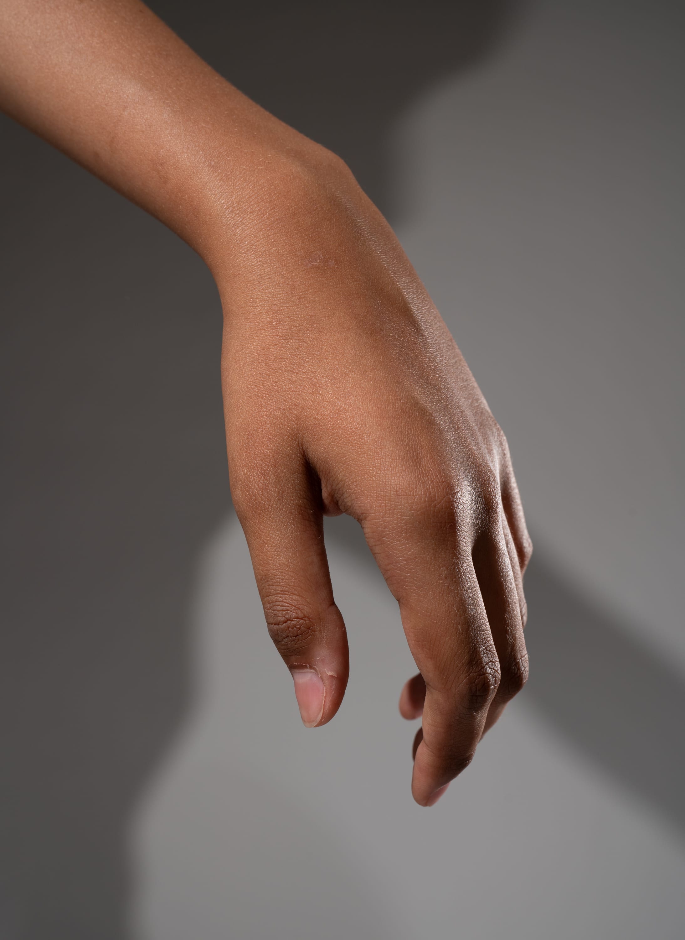 a closeup side view of a hand reaching downwards against a gray background with soft shadows.