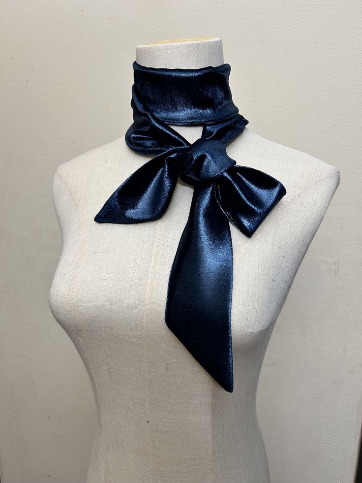 a closeup shot showcases a navy blue velvet choker scarf elegantly tied in a bow around a dress form's neck.  the fabric appears smooth and lustrous with a subtle shimmer. the choker is wide and substantial, suggesting a luxurious and sophisticated style. the dress form provides a neutral backdrop that highlights the scarf's rich color and texture.