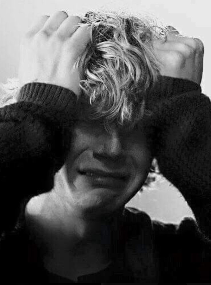 a black and white portrait of a man with blonde hair, crying. he is holding his hands over his face and is looking down. he appears to be very sad and depressed. the image is a close up and focuses on his face. the image is in black and white, which adds to the somber mood.