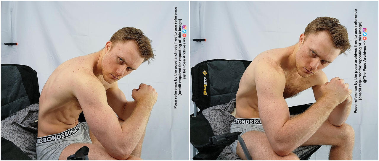 a shirtless muscular male with short brown hair sits in a chair in a studio setting, posing with his arm resting on his knee and fist clenched.