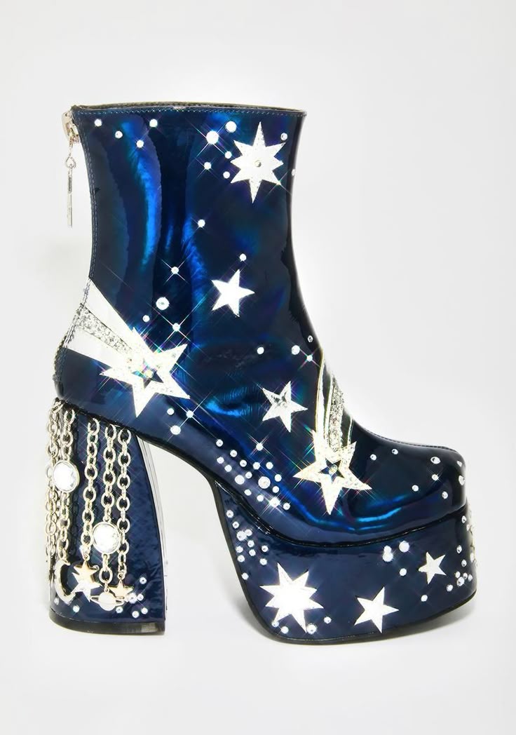 a shiny, dark blue platform ankle boot with a chunky heel is decorated with white stars and shooting star designs. the heel features silver chains with attached round and starshaped decorations, and a zipper is visible at the back of the boot.