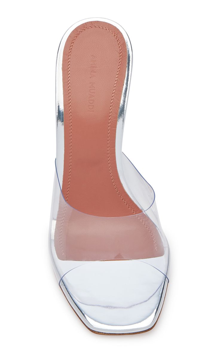 a topdown closeup shot of a pair of amina muaddi clear high heel mules. the shoes have a silver metallic trim and a blushcolored insole. the transparent pvc material allows the insole and heel structure to be seen.  the shoes are presented on a white background, typical of product photography for online retail.